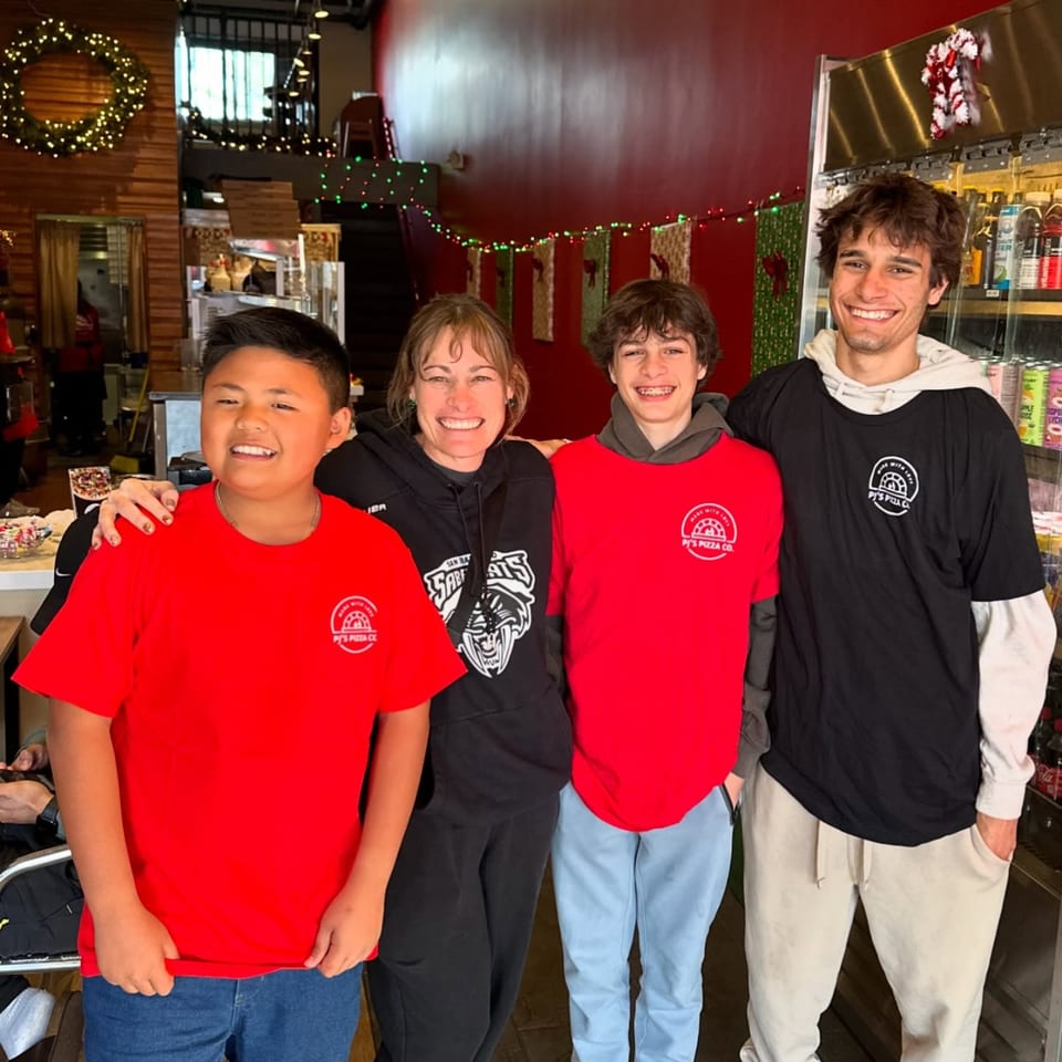 Four smiling Pj's Pizza Co. staff members, two in red shirts, one in black, and one in a hoodie.