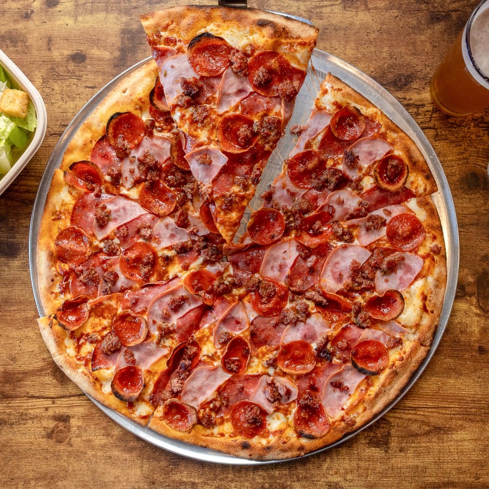 A Pj's Pizza Co. meat lover's pizza with pepperoni, ham, and sausage, with one slice removed.