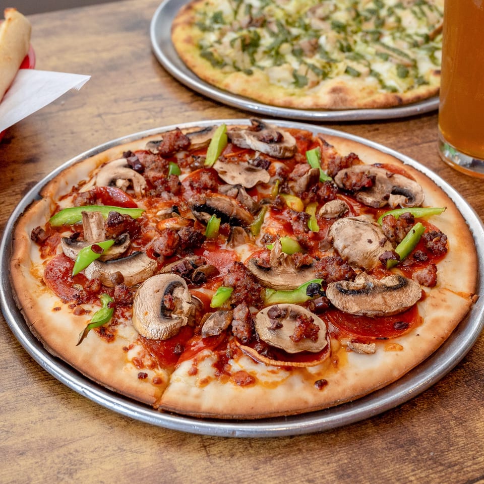 A Pj's Pizza Co. pizza with pepperoni, sausage, mushrooms, and green peppers on a wooden table.