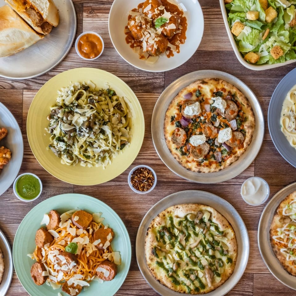 An overhead view of a wooden table laden with various Pj's Pizza Co. pizzas, pastas, and sides.