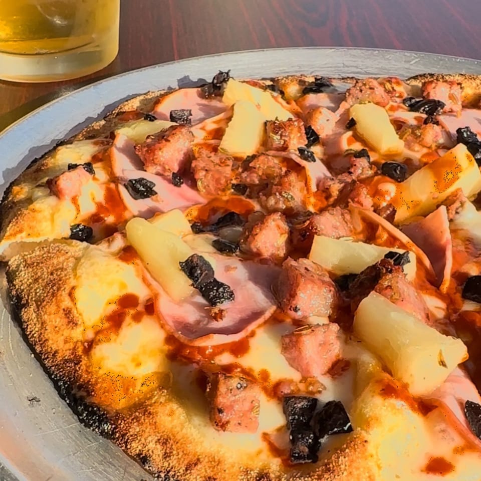 Close-up of a Pj's Pizza Co. pizza with ham, pineapple, and black olives.