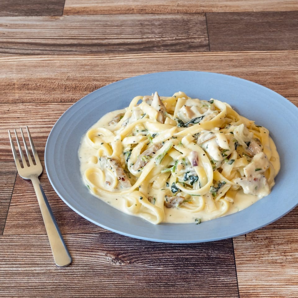 Creamy fettuccine pasta with chicken and spinach on a blue plate, with a fork beside it.