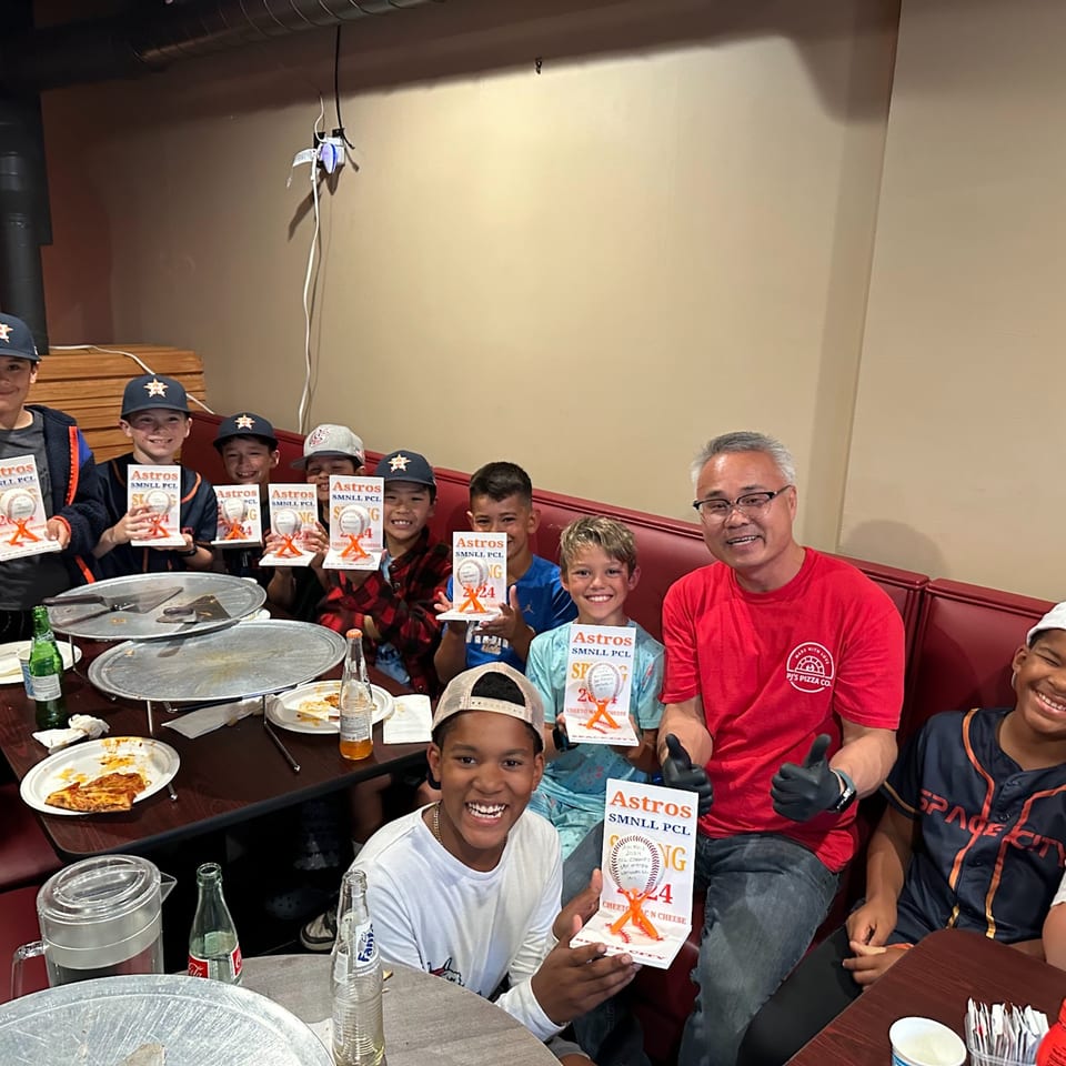 A group of young boys and an adult man, all smiling, holding awards at Pj's Pizza Co.