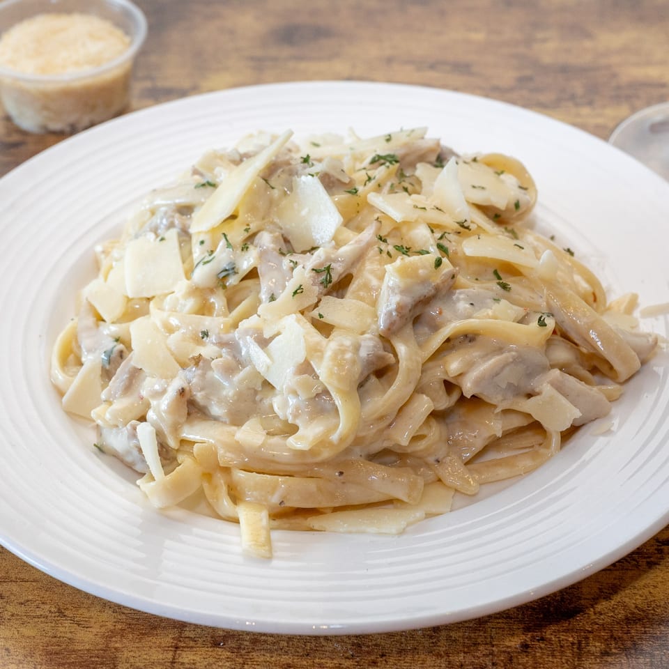 Creamy fettuccine alfredo with chicken, parmesan shavings, and parsley on a white plate.
