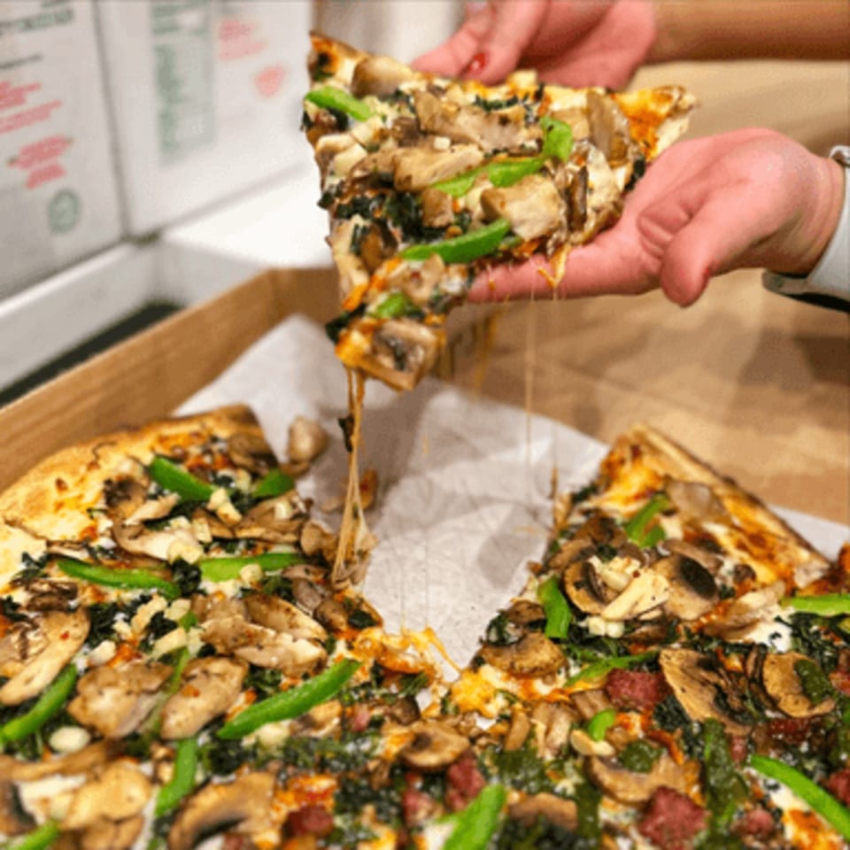 Hands pulling a cheesy slice of Pj's Pizza Co. pizza with mushrooms, green peppers, and spinach.